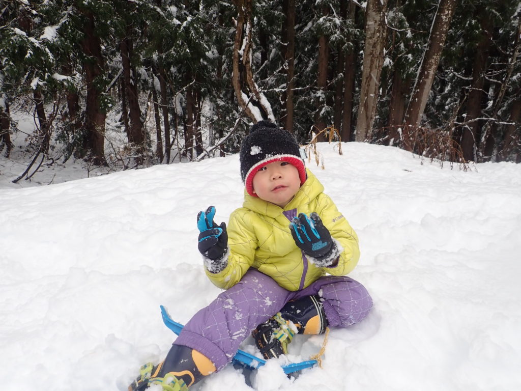 スノーシューを履いて雪の上に座る子供